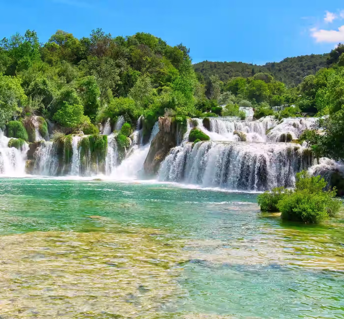 Drone Photography at Krka National Park, Croatia | Dazz Drones Sunny view of the Skradinski buk waterfalls in Krka National Park, Croatia, showing multiple cascades and vibrant green and turquoise water.