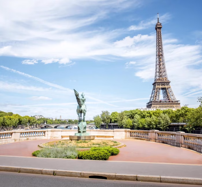 Eiffel Tower View in Paris, France | Iconic Landmark View of the Eiffel Tower in Paris, France, with a statue and trees in the foreground under a partly cloudy sky.