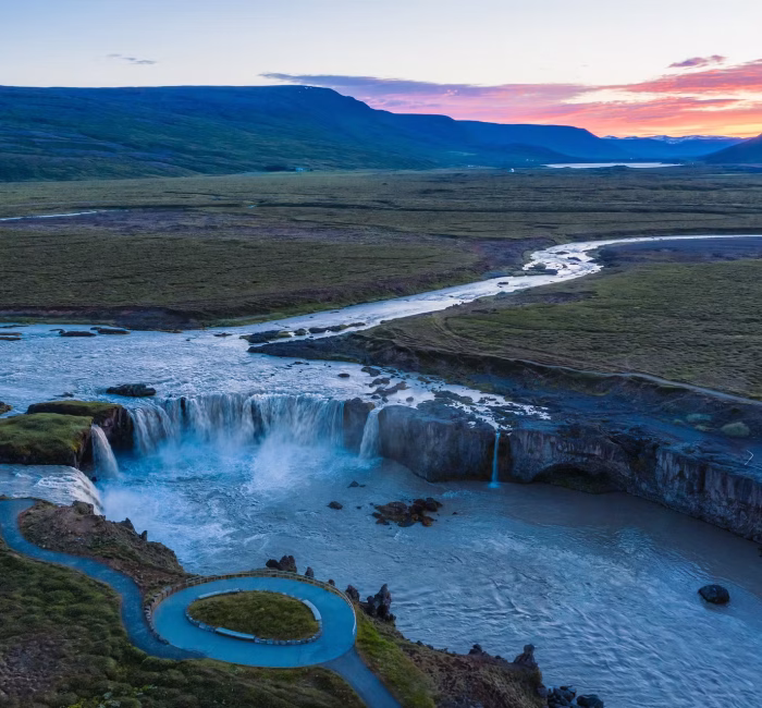 Aerial Drone Photography of Goðafoss Waterfall, North Iceland Aerial drone view of the wide, horseshoe-shaped Goðafoss waterfall in North Iceland during a colorful sunset or sunrise, surrounded by green landscape.