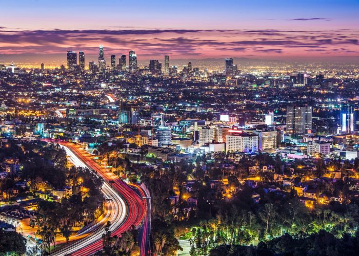 A vibrant night view of Los Angeles city skyline with illuminated buildings and busy highways, showcasing urban life.