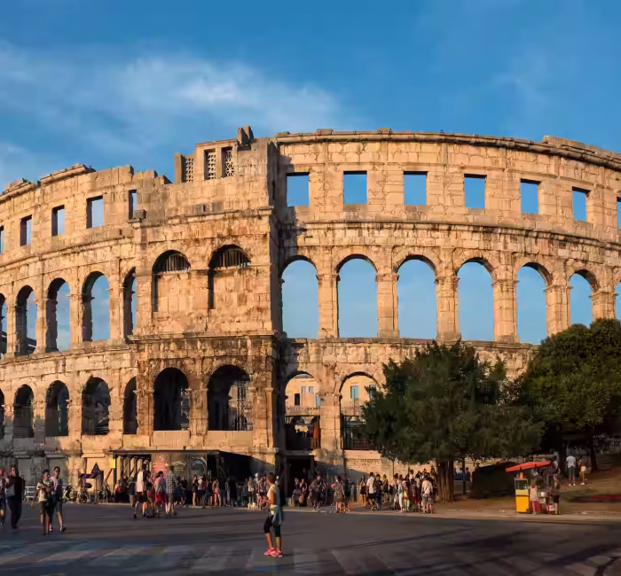 Drone Photography at Pula Arena, Croatia | Dazz Drones Exterior daytime view of the well-preserved Pula Arena, a large Roman amphitheater in Istria, Croatia, with tourists nearby.